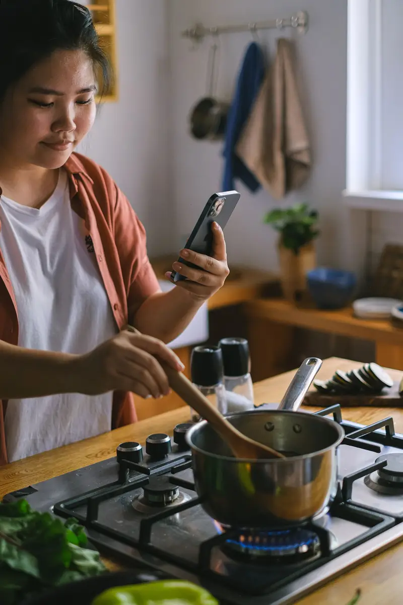 A woman cooking while using her phone